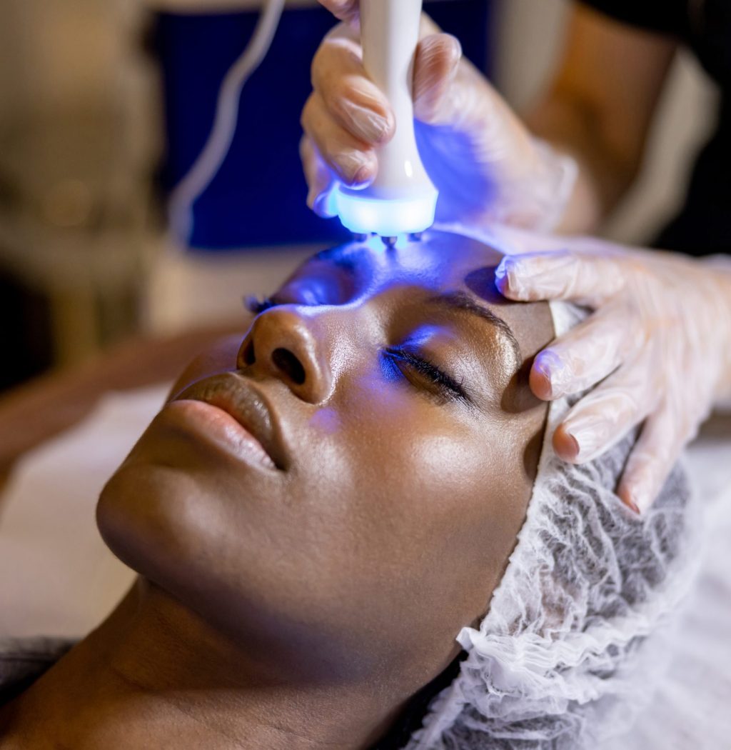 African American woman at the spa getting an ultrasound treatment on her face with blue light therapy